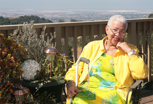 A woman sitting and smiling with a cane beside her.